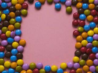 Top view of colorful chocolate candy with a frame in the center. Pink background