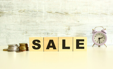 There are four wooden cubes with letters on the table next to the coins. SALE word. On a gray background.