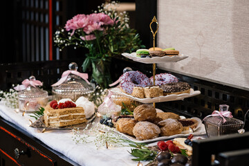 sweet table at the holiday. cakes with fresh berries, a two-tiered plate with donuts and profiteroles, flowers on the table