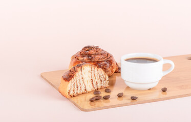 White cup with coffee, whole cinnamon bun and half bun on a cutting board.