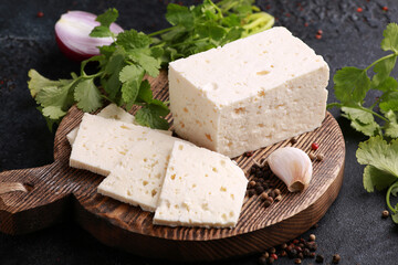 Homemade cheese with herbs, garlic, onions, spices on a wooden board on a black table. Goat cheese with coriander. Rustic. Background image, copy space