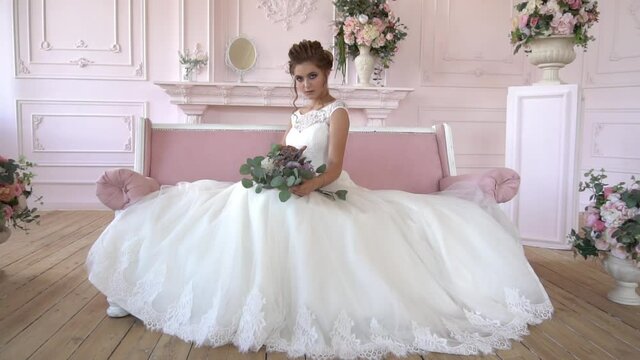 Slow Motion Beautiful Young Model In A White Lace Dress Sits On A White Bed. Gor