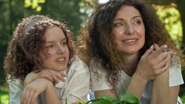 Spring portrait of mom and teenage daughter lying on the grass. Both look into the distance and smile. Mothers Day.