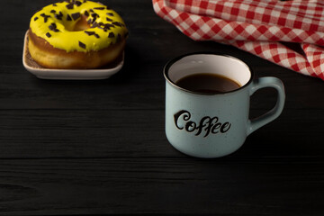 coffee time. A cup with the inscription stands on a black wooden background. Donut with pink icing on the back. High quality photo