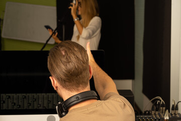 Caucasian young musical performance singer recording in creative studio with producer 