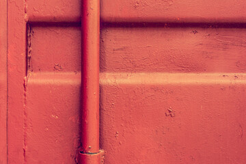 Metal wall with a pipe covered with red paint