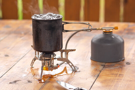 Water is boiling in a metal mug. The mug stands on a gas camping stove