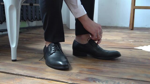 Slow Motion Man ties the laces on black shoes. Close-up of hands and shoes