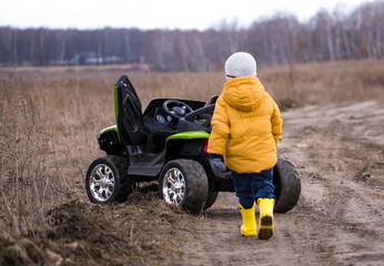 a two-year-old child rides his car on a field in the fall