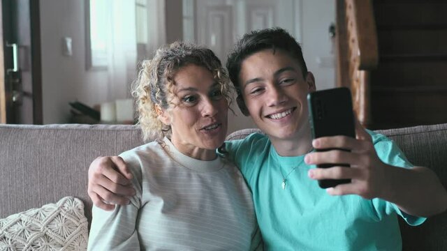 Smiling middle-aged 40s mother rest with grown-up son using smartphone together, happy young man enjoy family weekend with mom browsing wireless Internet on cellphone, have fun at home
