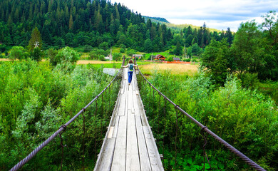 Fototapeta premium cable bridge,wooden bridge. The girl goes along the rope wooden bridge. Amazing wooden rope bridge over a river