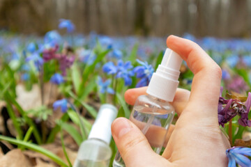 Hand spray clear liquid pump bottle in blooming spring flower lawn of blue Scilla bifolia (squill)....
