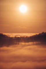 Glowing orange ball illuminates floating clouds around the mountains in spring time. Walking above the clouds at sunset. Orange tone of the whole image