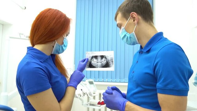 Dentist doctor holding teeth x-ray and nurse taking notes on clipboard in stomat