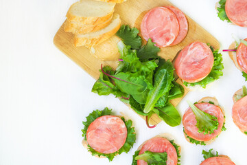 Cream cheese sandwiches with red fish, baguette, iceberg lettuce leaves, swiss chard on wooden board, top view, copy space. Sandwiches on white background