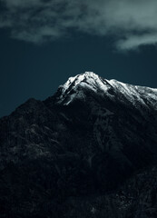 Vertical shot of a rocky mountain covered with snow under a cloudy sky