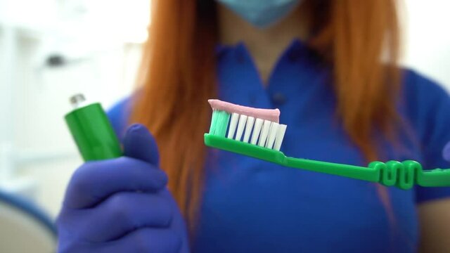 Friendly dentist showing toothpaste and toothbrush. Smiling stomatologist in modern dental office. Portrait of beautiful woman dentist holding whitening toothpaste
