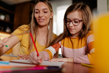 Fototapeta premium Mom and child creating beautiful picture, using color pencils at home. Focus on little girl.
