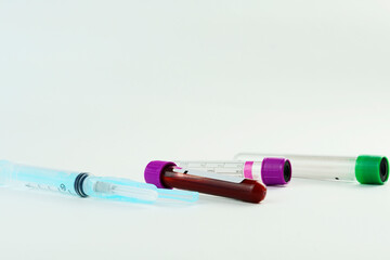 Vacuum tubes for collection and blood samples and a syringe on white background. Transparent tubes with purple and green lid. Label to identify the data. Selective focus.
