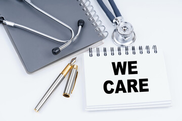 On the table are a stethoscope, a pen and a notebook with the inscription - WE CARE
