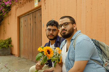 Retrato frontal de pareja de novios gay con barba sosteniendo flores amarillas 
