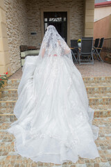 The bride takes a photo of the wedding dress from behind at home . the bride in a luxurious white dress stands near the window . The back side of a white wedding dress .