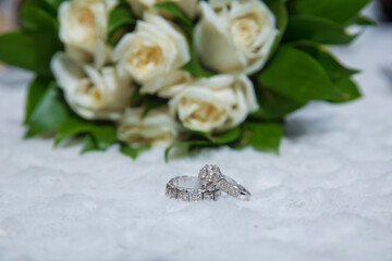 Wedding engagement rings on the background of a beautiful bouquet of roses . Stylish white wedding flower Rings in front of the wedding bouquet .