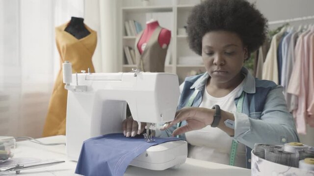 Black seamstress looking at watch, sewing fabric in tailoring studio, deadline