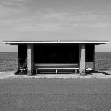 A black and white photograph showing a couple sit talking in one of the seafront seating booths in Llandudno Bay