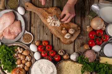 The chef prepares a mushroom salad. Many bright, colorful ingredients - tomatoes, eggs, duk, herbs, spices, sour cream. Nice angle. Wooden cutting board and wooden table