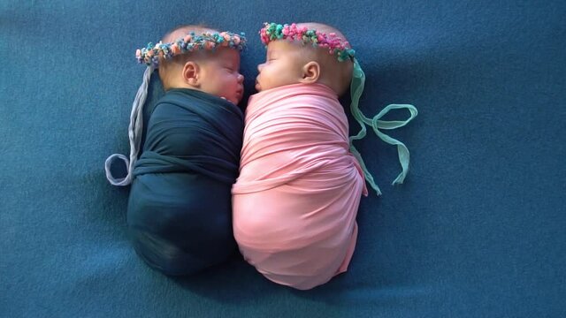 Headshot of fraternal twin newborn baby girls swaddled in pink and blue stretch 