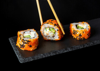Traditional sushi and chopsticks. Philadelphia with salmon, avocado and cheese. Japanese cuisine on black background