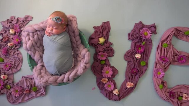 Little sleeping newborn girl surrounded by flowers. lettering from flowers love