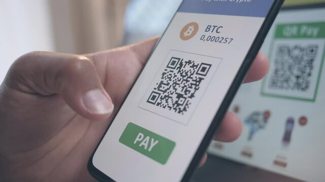Close up of a smartphone scanning QR code on a laptop monitor, visible in the background, payment with crypto wallet mobile app