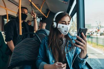 Young woman using a smartphone and wearing protective maskin the bus