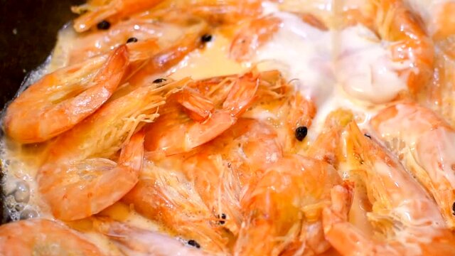 Close-up of shrimps being fried in cream. seafood, cooking process, healthy eating concept. Shef puring cream on shrimps.