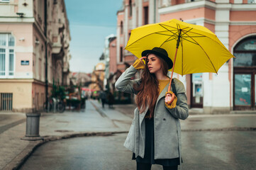 Young beautiful woman waiting for a cab and holding a yellow umbrella outside
