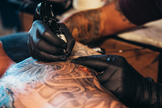 Tattoo artist hands wearing black gloves while holding a machine