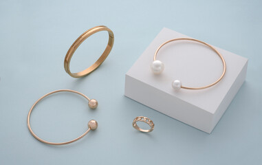 Collection of golden bracelets and ring on white box on blue background