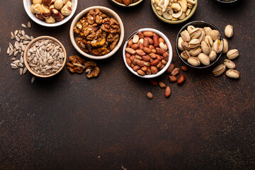 Obraz na płótnie Canvas Selection of assorted raw nuts and various seeds in bowls on brown stone background from above, healthy source of energy, fat and vegetarian protein, space for text