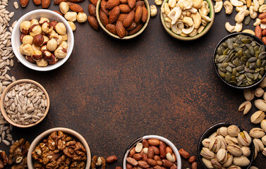 Selection of assorted raw nuts and various seeds in bowls on brown stone background from above, healthy source of energy, fat and vegetarian protein, space for text