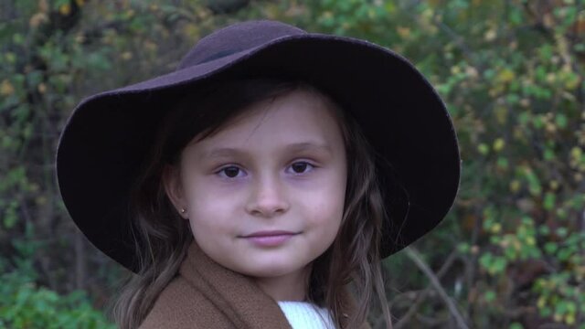 Portrait of cute kid girl wearing a hat autumn season beautiful trees background