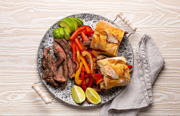 Fajitas sandwiches made from traditional Mexican dish Beef fajita and white bread served with ripe avocado on white wooden rustic background from above, American Mexican food healthy snack