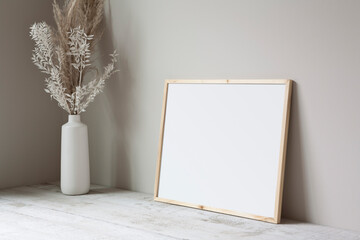 16x20 thin wooden, horizontal frame mockup, lying on a white wooden floor with a pampas grass prop.