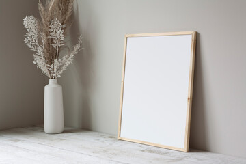 16x20 thin wooden, vertical frame mockup, lying on a white wooden floor with a pampas grass prop.