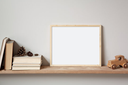 11x14 thin wood horizontal frame mockup for art and quotes, sitting on a wooden shelf. Vintage stack of books, old toy car and pine cones as props.