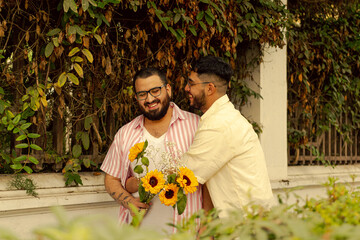 Joven gay con barba abraza a su novio en la calle mientras sostiene un ramo de flores amarillas 