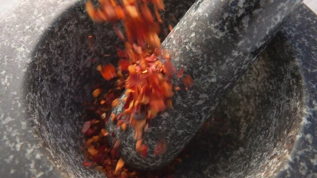 Close-up of the red hot chilli peppers falling into the stone mortar