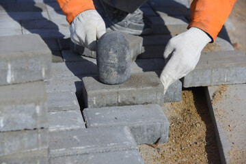 A worker knocks on paving slabs, levels a concrete block with a construction hammer, repairs a pedestrian road.