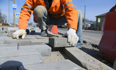 A worker lays paving slabs, builds a road for pedestrians.The builder is laying concrete blocks in the sand in straight rows.
